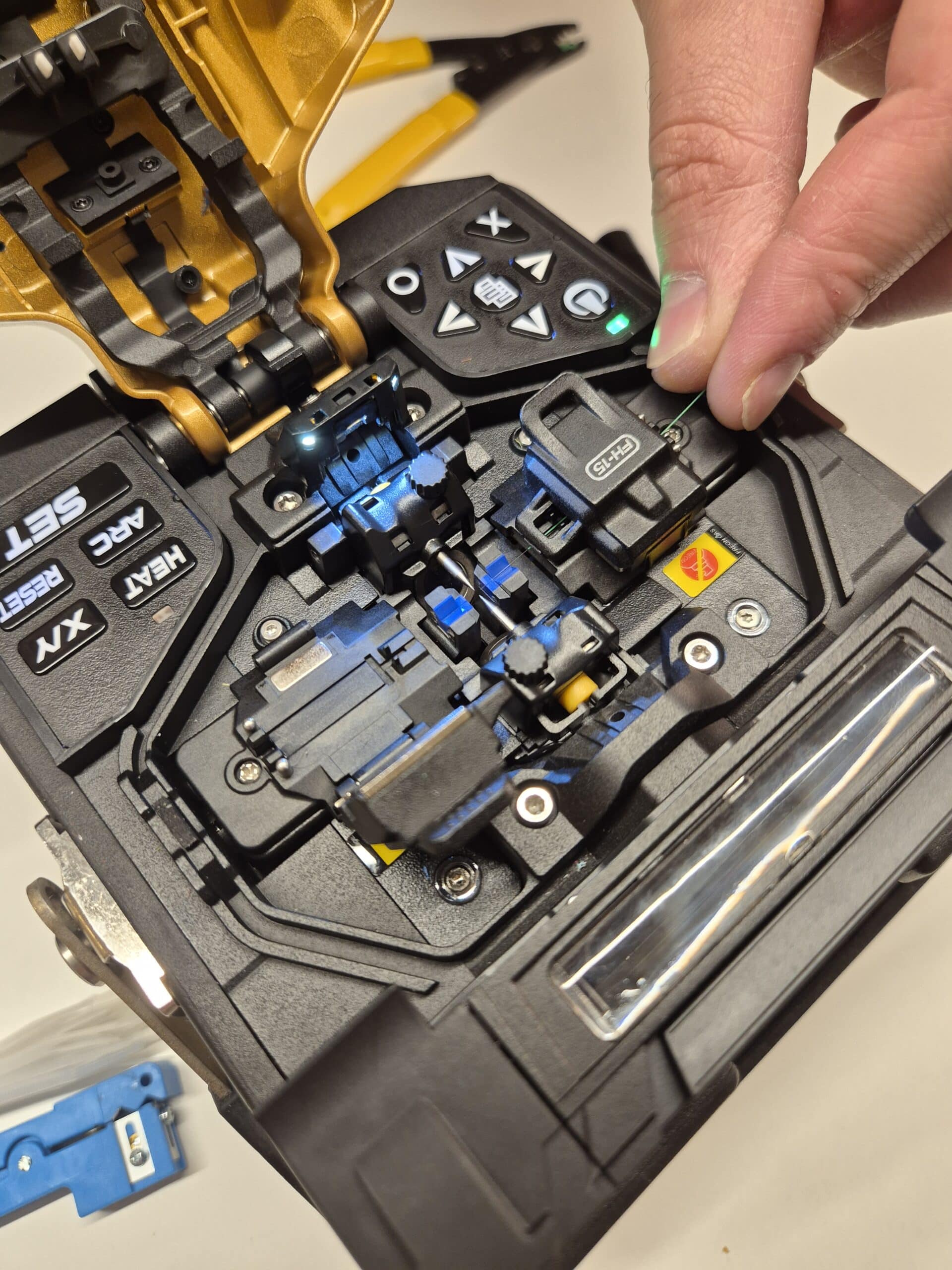 Nahaufnahme einer Hand, die präzise eine Glasfaser in die Halterung eines geöffneten INNO View Fusions-Spleißgeräts einlegt.